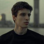 Portrait of a young man with a city skyline at twilight, capturing a moody and contemplative atmosphere.