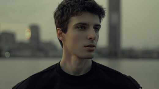 Portrait of a young man with a city skyline at twilight, capturing a moody and contemplative atmosphere.