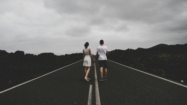A couple walks hand in hand on an open road in Lanzarote, Spain, under a cloudy sky.