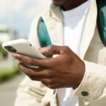 Close-up of a person using a smartphone outdoors, wearing a jacket and backpack.