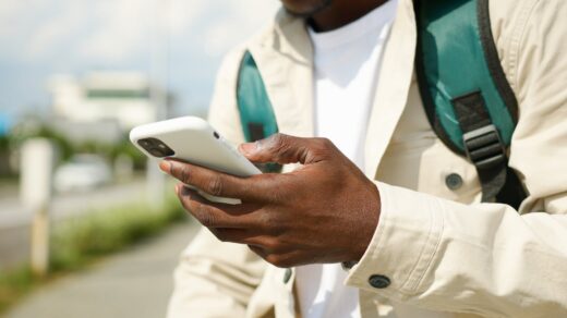 Close-up of a person using a smartphone outdoors, wearing a jacket and backpack.