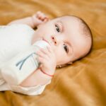 baby in white dress lying on yellow textile