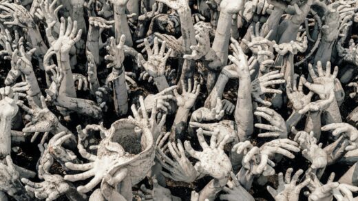 Many hands reach upwards in a sea of grey.