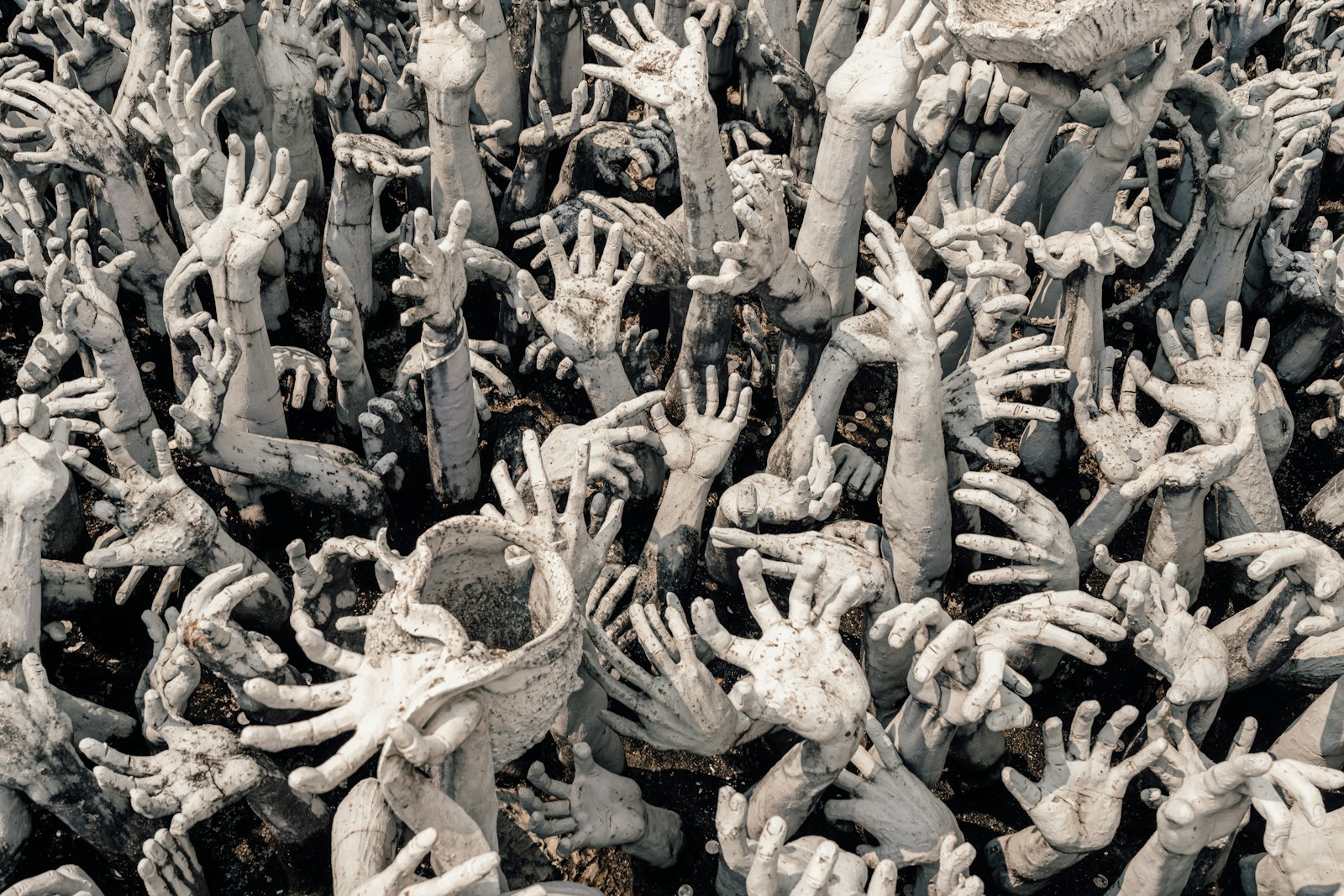 Many hands reach upwards in a sea of grey.