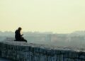 woman in black jacket sitting on gray concrete wall during daytime