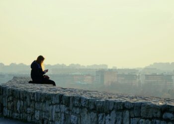 woman in black jacket sitting on gray concrete wall during daytime