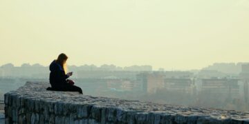woman in black jacket sitting on gray concrete wall during daytime