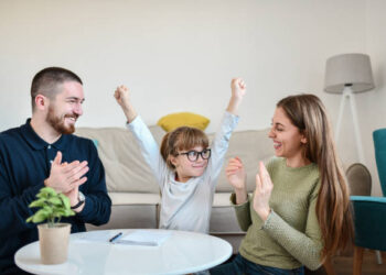 Smiling Female Child Showing Success While Writing Homework In Front Of Parents