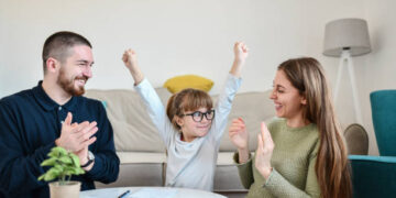 Smiling Female Child Showing Success While Writing Homework In Front Of Parents
