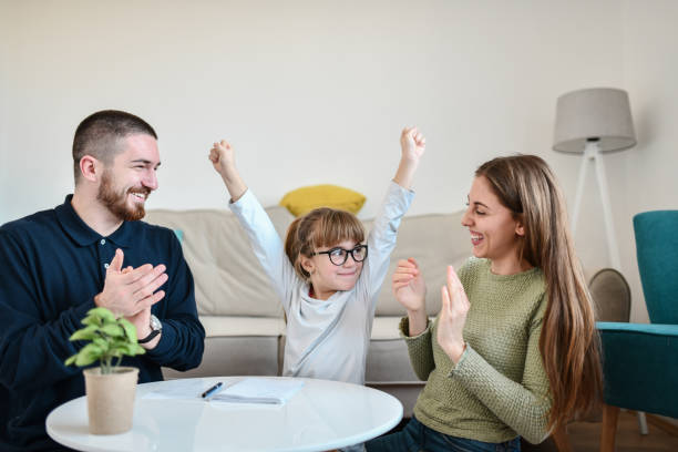 Smiling Female Child Showing Success While Writing Homework In Front Of Parents